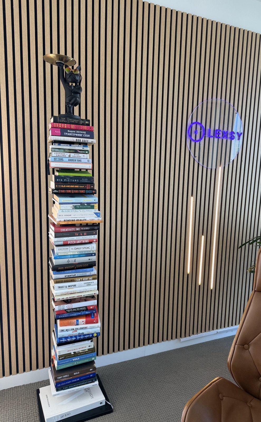 A tall stack of business, startup and philosophy books on a stand against a slatted wood wall at the Lexsy office